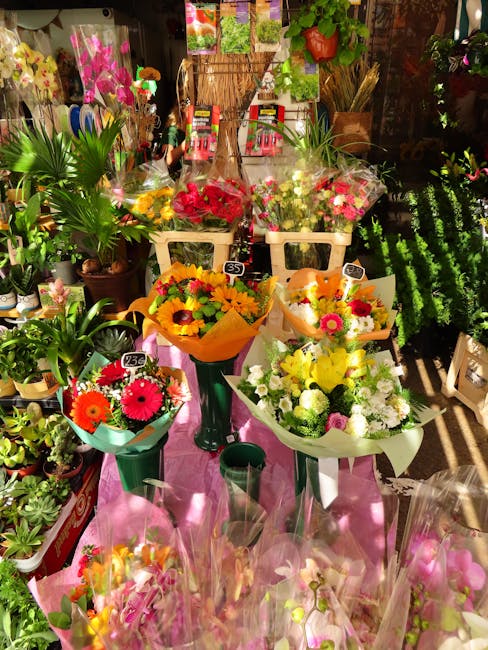 A display of fresh floral bouquets arranged on tall green stands and a pink table within a flower shop, featuring a variety of colorful blooms including bright yellow sunflowers, pink gerbera daisies,